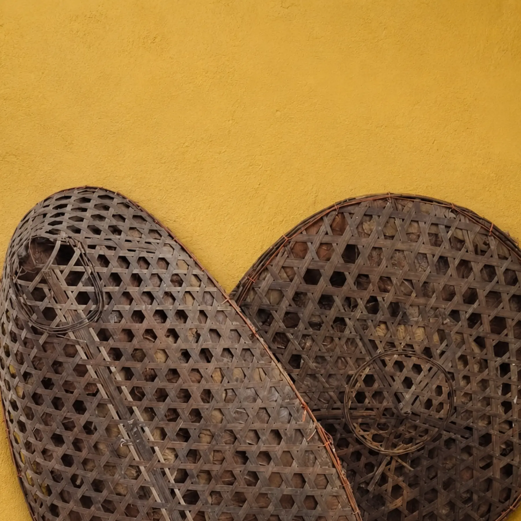 Woven bamboo winnowing implements mounted on a yellow wall