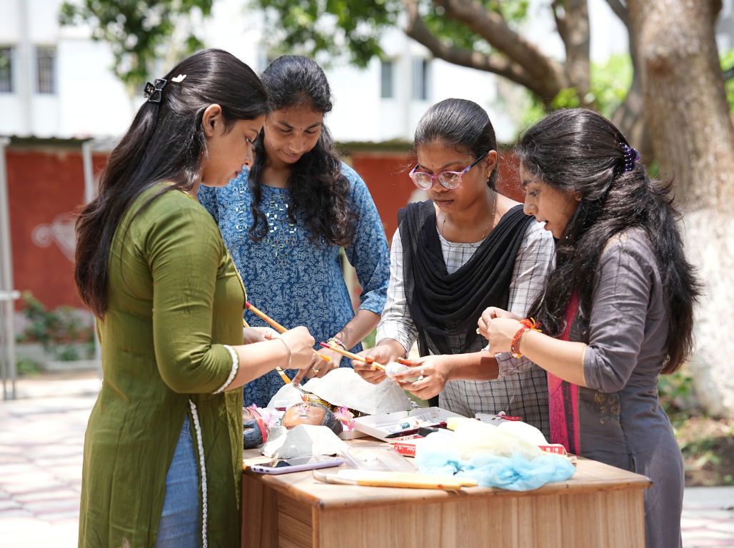 Young women painting a clay idol together at an outdoor craft workshop