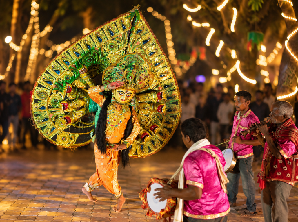 A Chhau dancer in a large green and gold headdress with drummers alongside