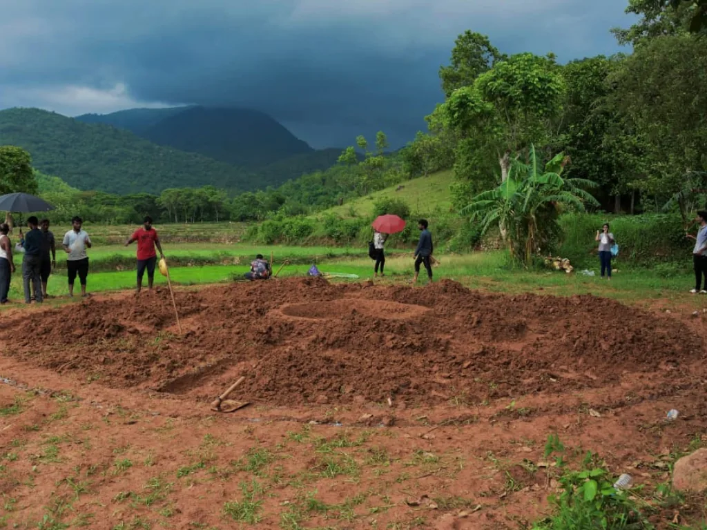 Field team observing a landscape model with hills and monsoon clouds in the background