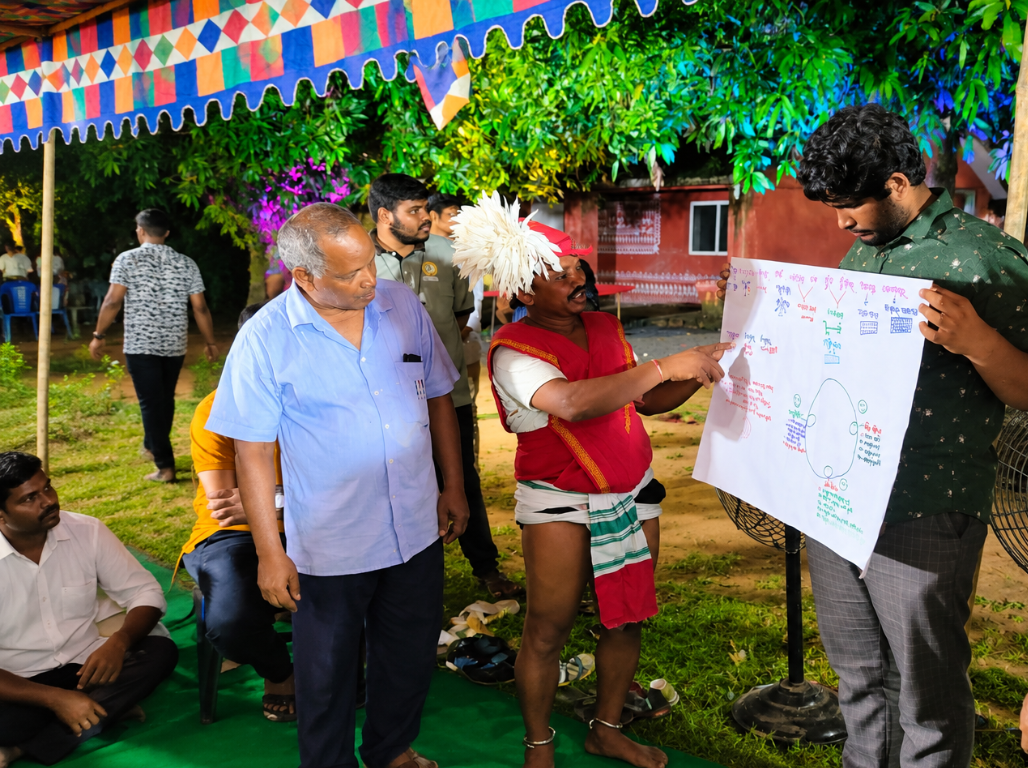 A facilitator holding a hand-drawn chart while a community elder explains it during a village learning camp