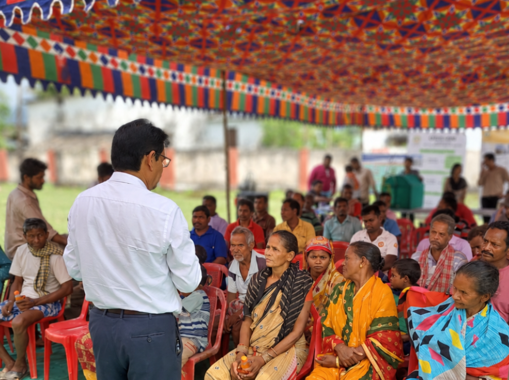 A facilitator addressing seated farmers under a colourful canopy at an agriculture scheme camp