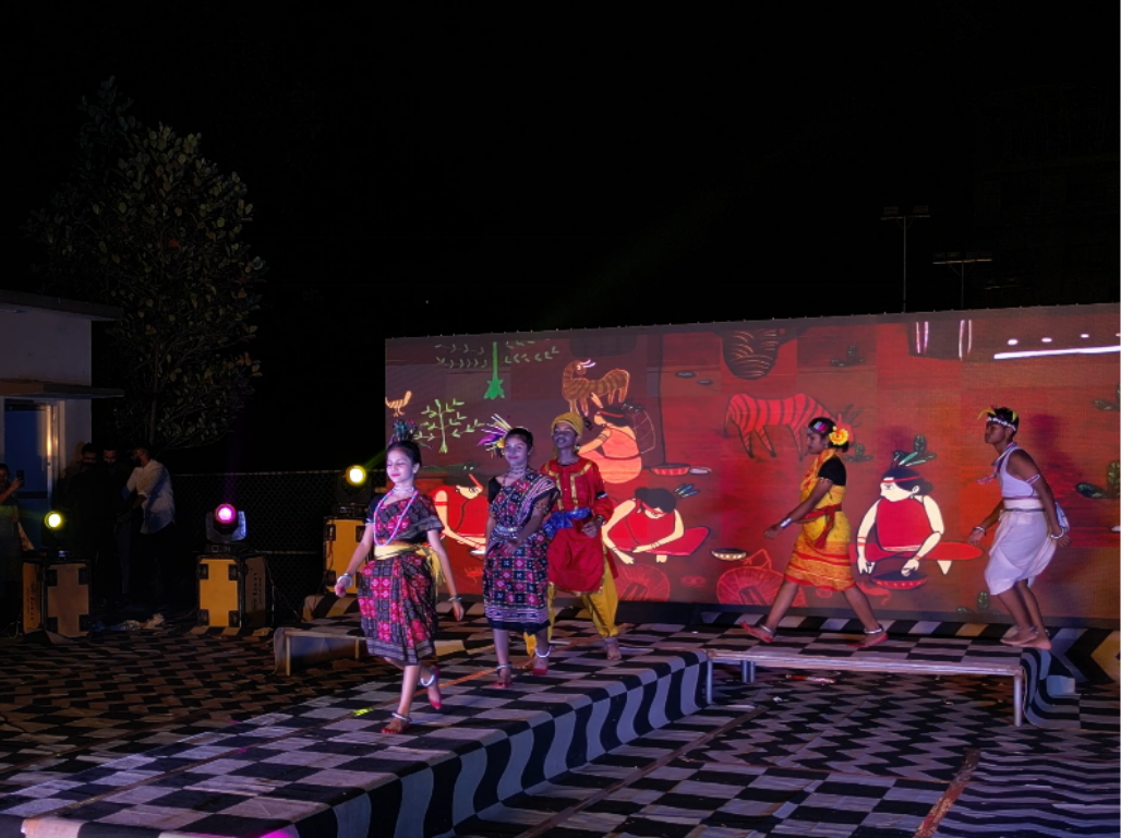 Models walking a lit ramp in Sora traditional dress before a painted tribal mural