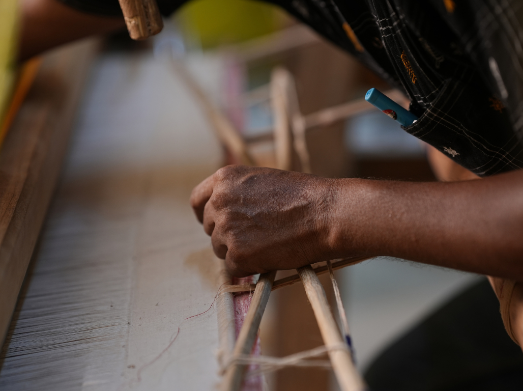 Close-up of a weaver's hand setting the warp on a traditional loom