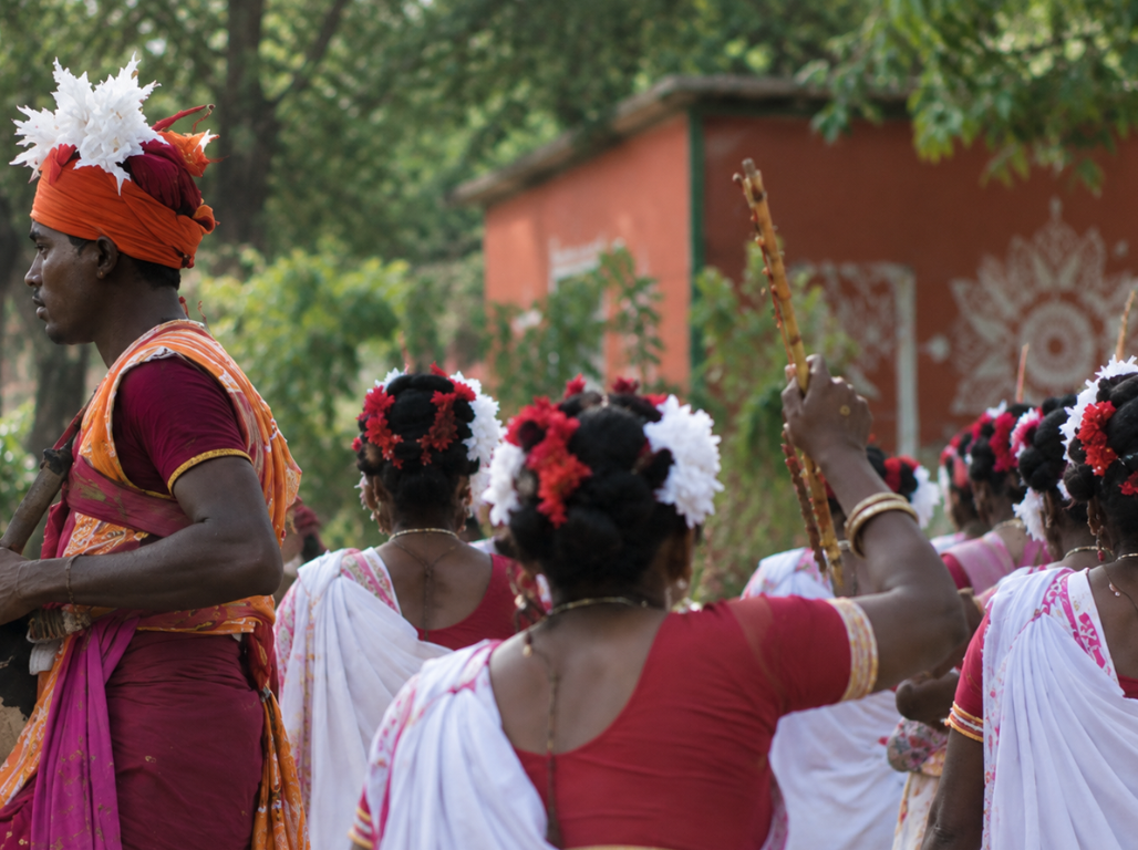 Dancers in white and red saris with floral headpieces moving in procession