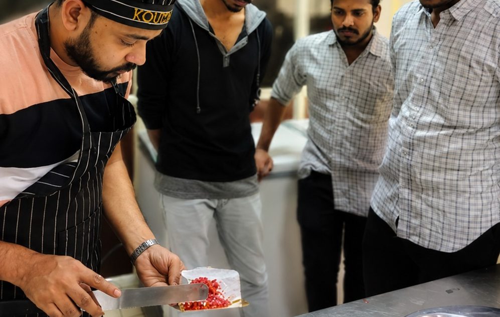 A chef demonstrating knife work on a garnish while trainees watch