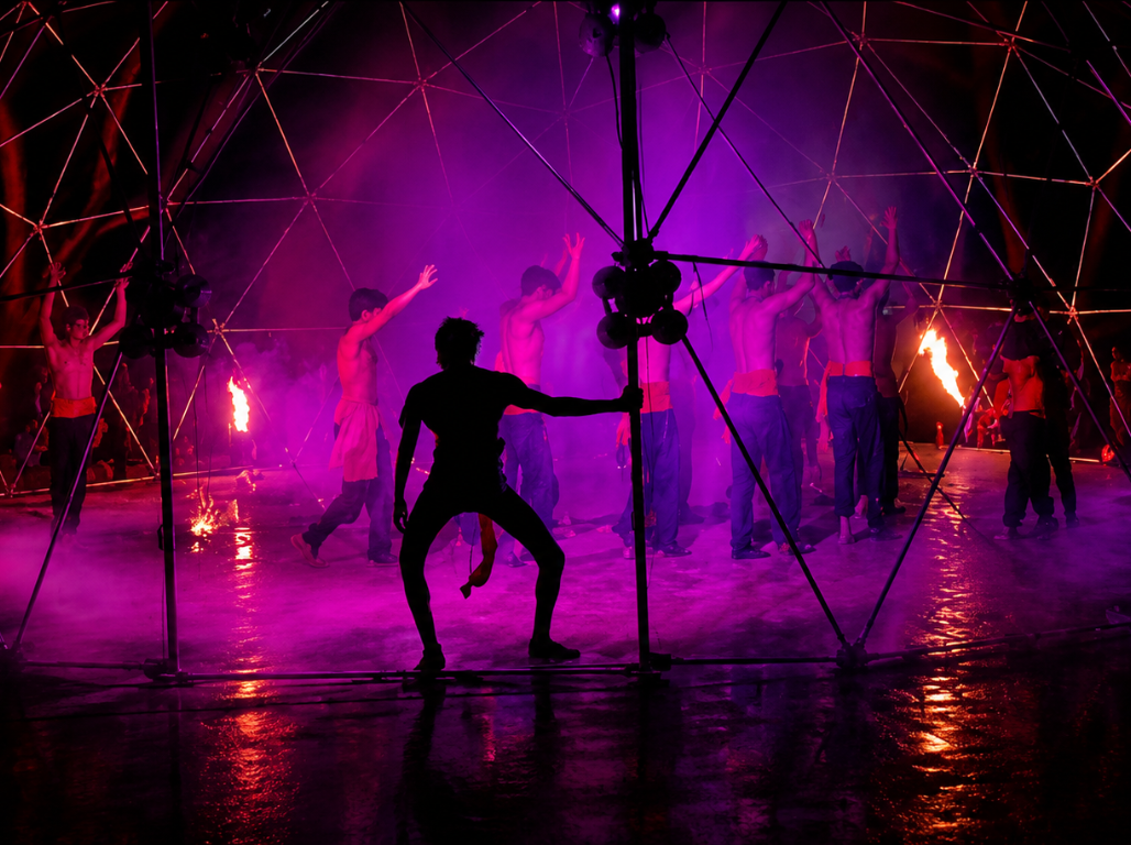 A dramatic stage performance lit in magenta light with fire torches
