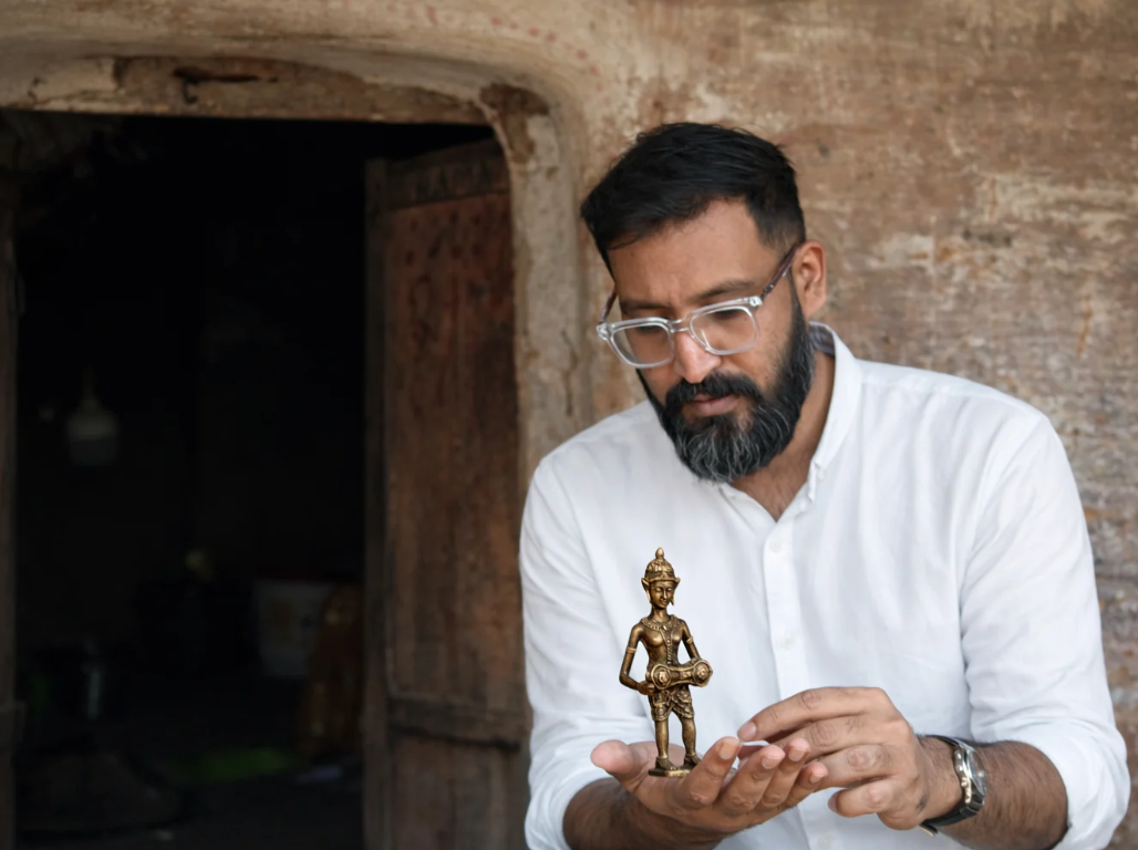 A man examining a small brass dokra figurine outside a village workshop