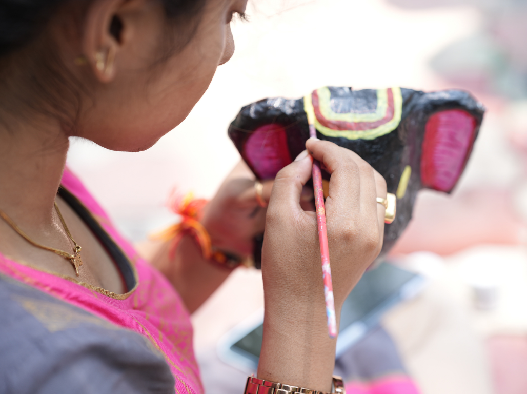 Close view of a young woman painting a black and pink mask with a fine brush