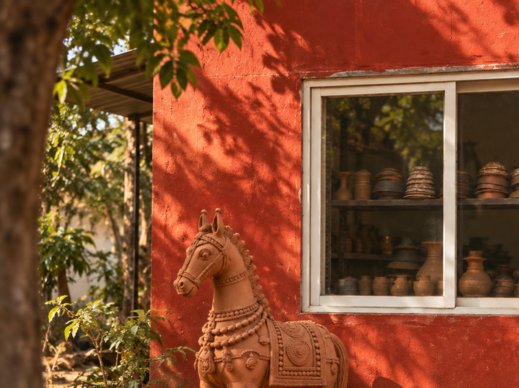 A terracotta horse standing beside a red studio wall of fired pots