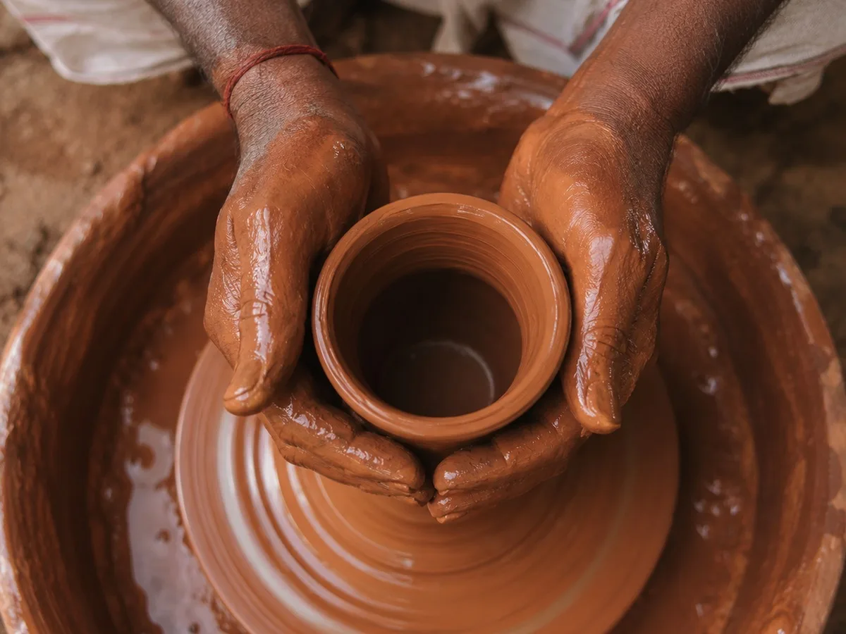A potter's hands shaping a clay pot on a spinning wheel