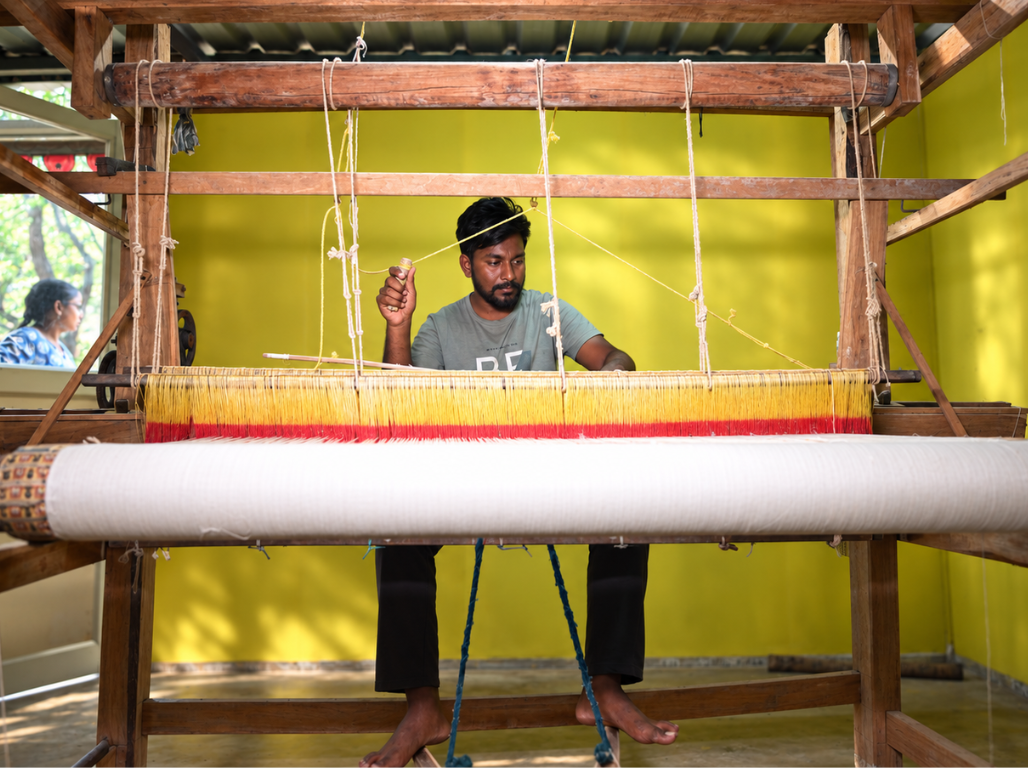 A weaver at a handloom with yellow and red warp threads