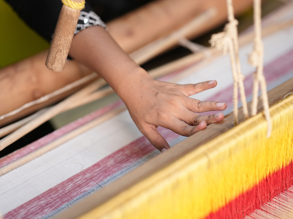 Weaver's hand working coloured warp threads on a loom
